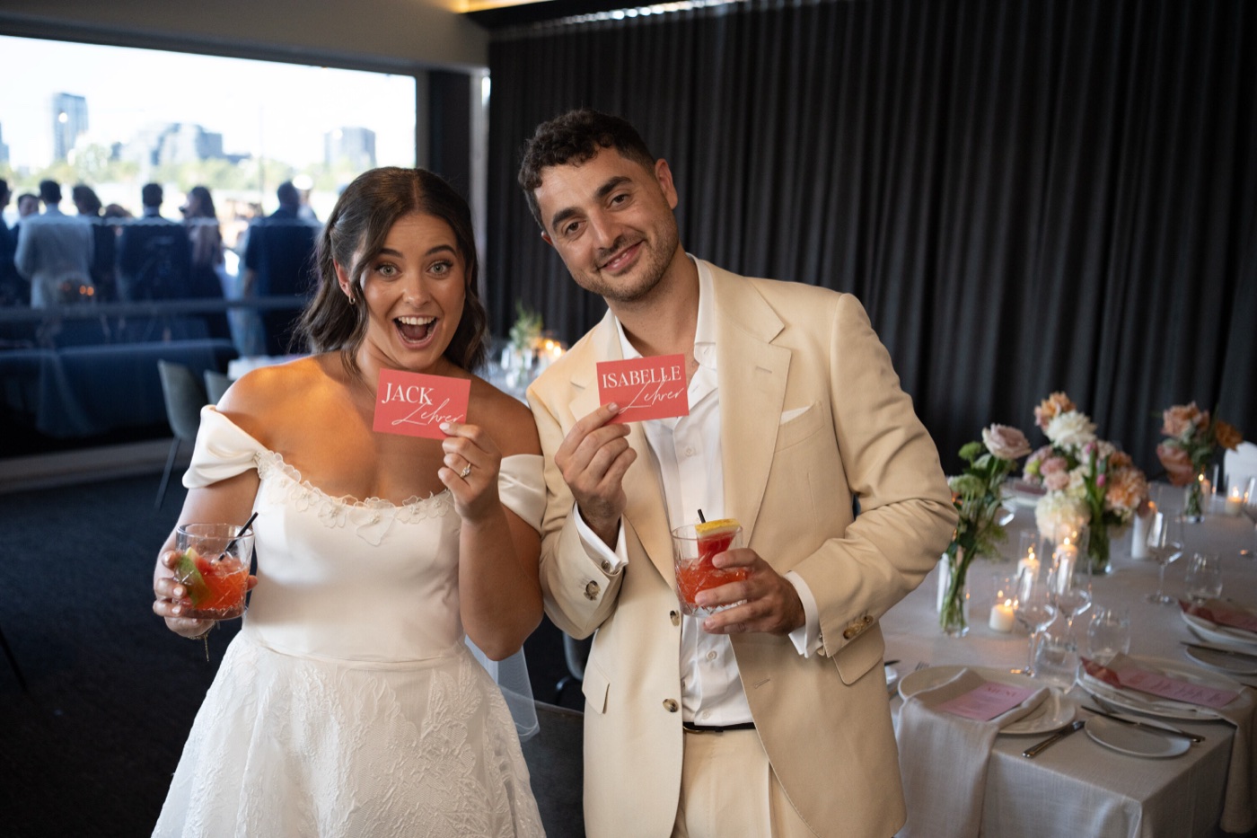 The couple holding each other's place cards, cocktails in hand