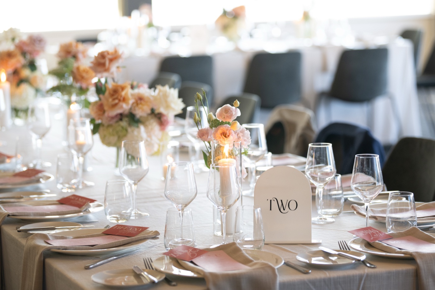 A round table dressed with peach roses, candles and an arched table number