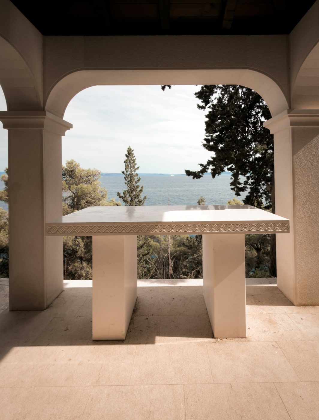 A stone arch framing the sea above a marble table on a villa terrace