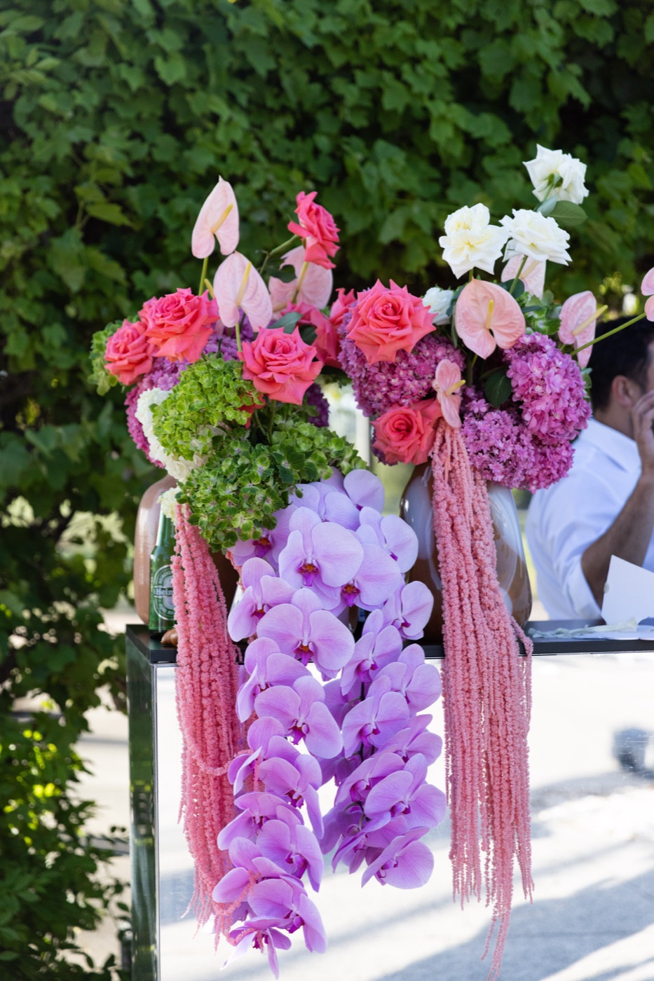 A cascading arrangement of orchids, roses and amaranthus on a mirrored plinth
