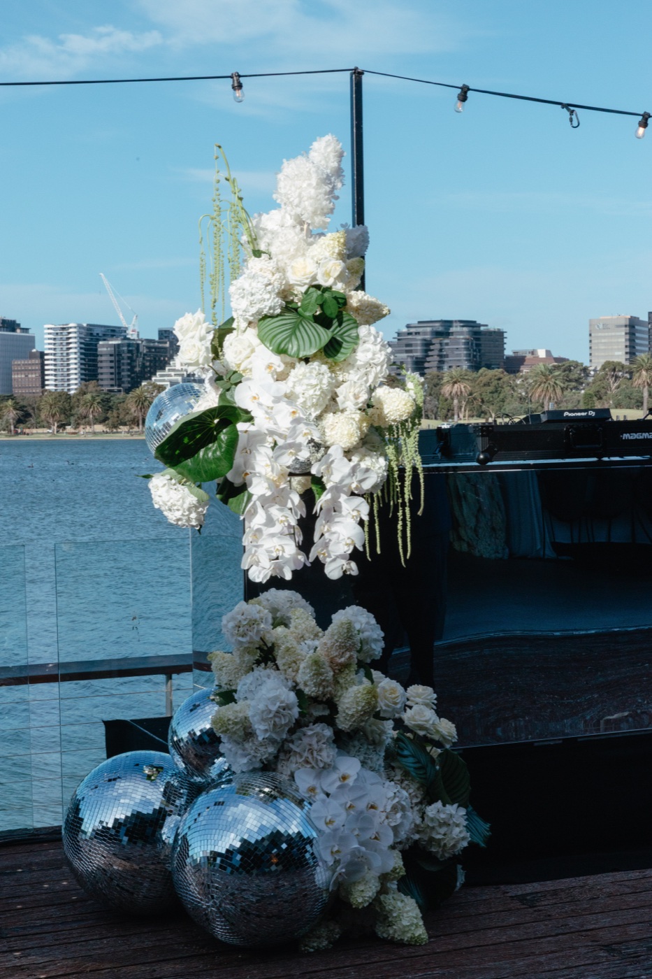 A white floral installation beside the booth, disco balls at its base, the lake and city behind
